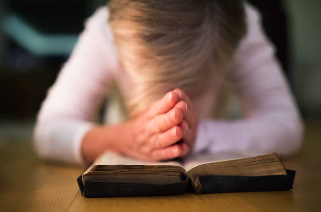 Unrecognizable woman praying with hands clasped together on her Bible. Close up.