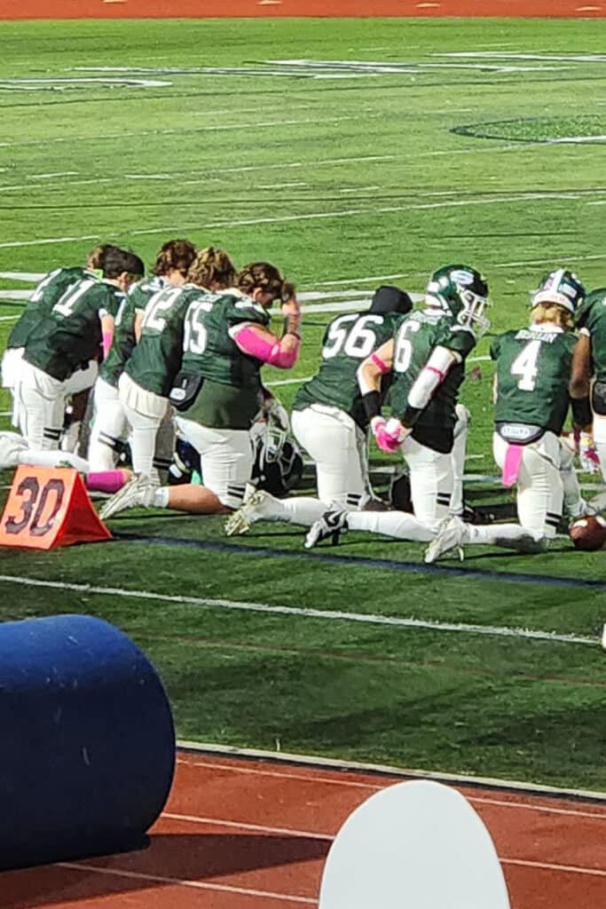 High school football players on the sidelines praying.